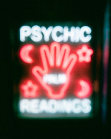 A neon sign featuring the words 'Psychic Readings' with a central image of a hand surrounded by symbols like crescent moons and stars.