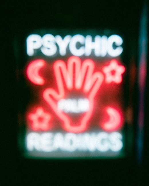 A neon sign featuring the words 'Psychic Readings' with a central image of a hand surrounded by symbols like crescent moons and stars.