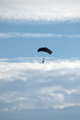 A parachutist gracefully descending against a clear blue sky.