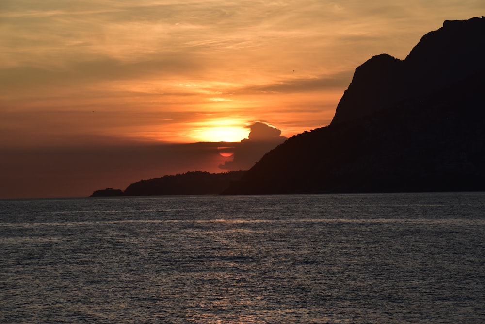 the sun is setting over the ocean with mountains in the background