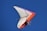 A hang glider with vibrant orange and purple accents soars against a clear blue sky. The pilot and a passenger are securely strapped in the harness, wearing helmets for safety.