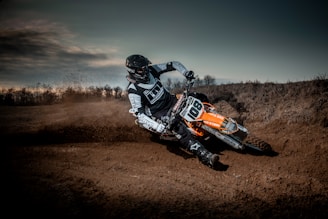 A close-up shot of a motocross rider kicking up dirt on a rugged forest trail under moody, overcast skies.