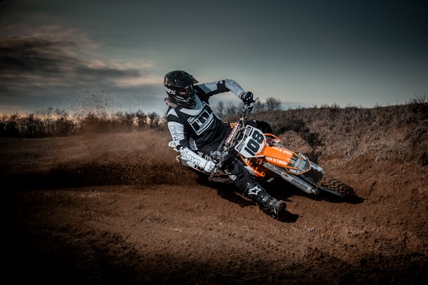 A close-up shot of a motocross rider kicking up dirt on a rugged forest trail under moody, overcast skies.