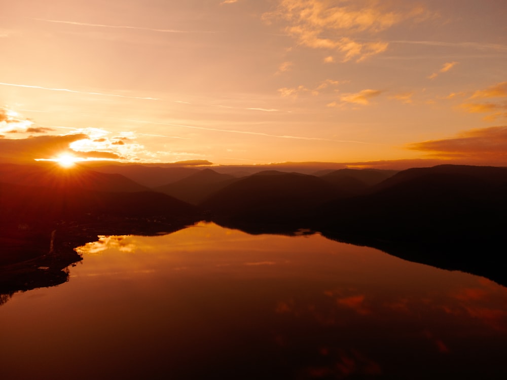 the sun is setting over a lake with mountains in the background