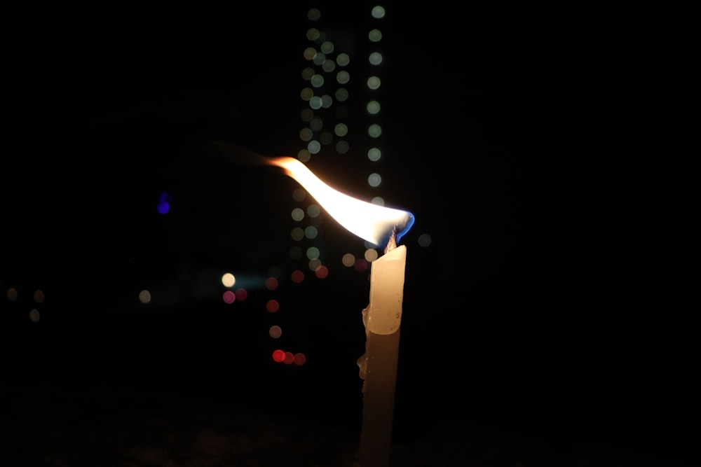 a lit candle in the dark with blurry lights in the background
