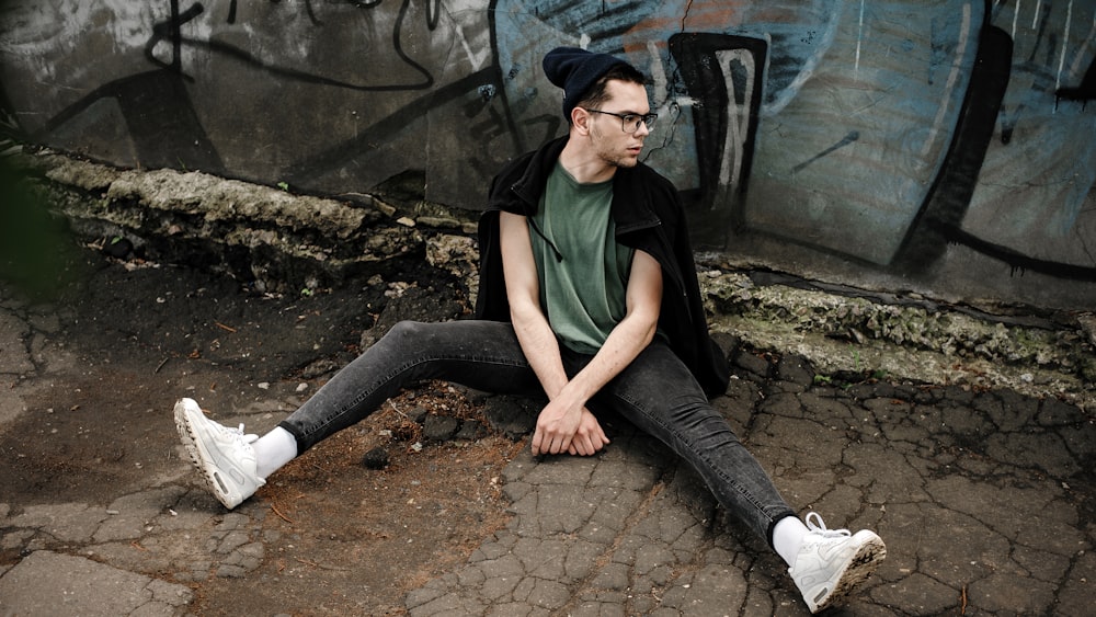 a man sitting on the ground in front of a graffiti covered wall