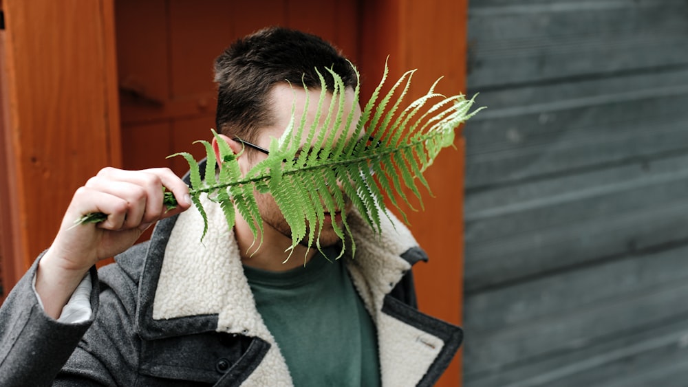 a man holding a fern leaf over his face