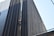 A person in bright safety gear is performing maintenance or cleaning work on a modern building's exterior. The structure features tall, vertical lines made of dark metallic or glass material, creating a striking visual contrast with the person.