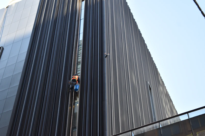 A climber in safety gear working on a tall building facade at sunset.