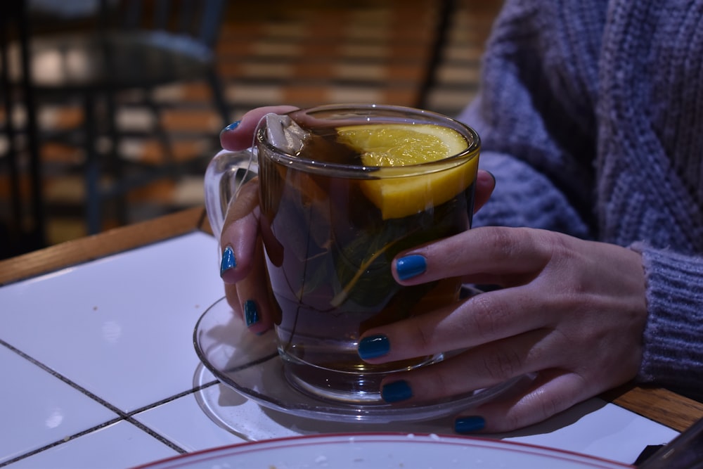 a woman holding a cup of tea with a lemon slice