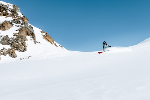 A snowboarder carving fresh powder on a sunlit mountain slope, with crisp blue skies above.