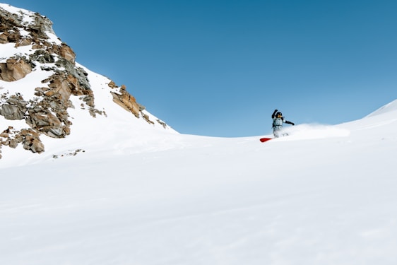 A skier carving fresh powder on a pristine snowy mountain slope under a clear blue sky.