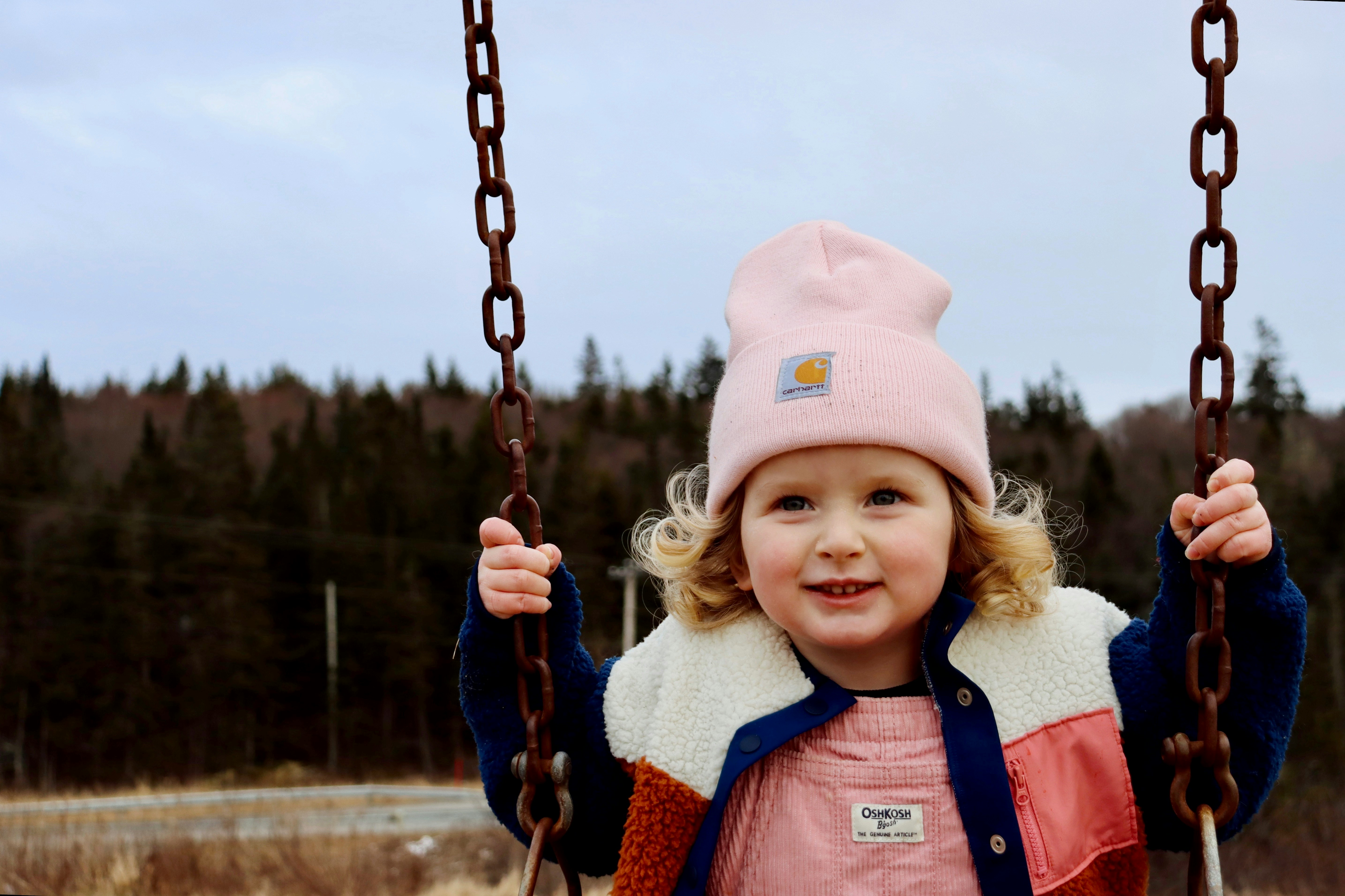 a little girl in a pink hat is on a swing