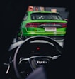 a green car driving down a street next to a person