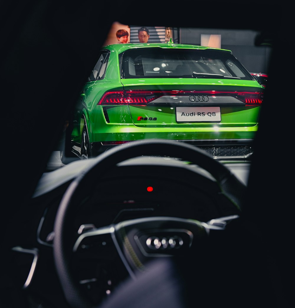 a green car driving down a street next to a person