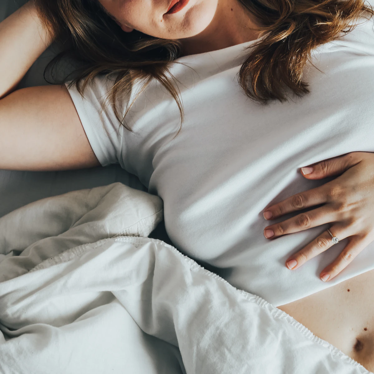 Adult woman in white resting calmly on soft white sheets