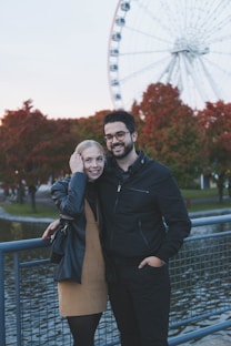 a man and a woman posing for a picture in front of a ferris wheel