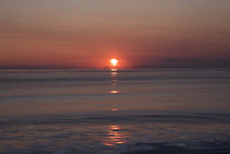 A serene ocean horizon at sunset with gentle waves reflecting warm colors.
