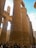 Massive ancient stone columns with intricate hieroglyphic carvings dominate the scene. Several tourists stand at the base, looking up and taking pictures. The architecture exudes a sense of history and grandeur, characteristic of ancient Egyptian temples.