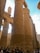 Massive ancient stone columns with intricate hieroglyphic carvings dominate the scene. Several tourists stand at the base, looking up and taking pictures. The architecture exudes a sense of history and grandeur, characteristic of ancient Egyptian temples.