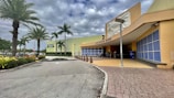 An outdoor view of a shopping center with prominent palm trees lining the pathway. The complex has a large sign for Old Navy Outlet and Dolphin Mall, with modern architectural design elements and a cloudy sky overhead.