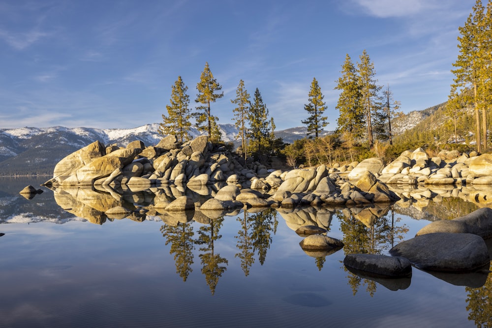 a lake surrounded by rocks and trees with mountains in the background