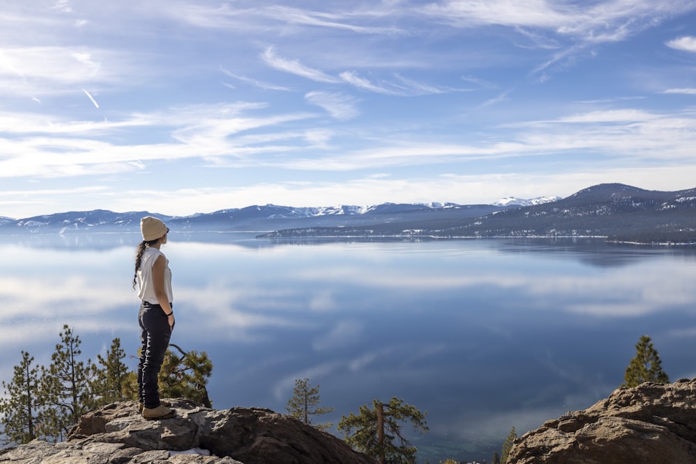 a woman standing on top of a mountain overlooking a lake