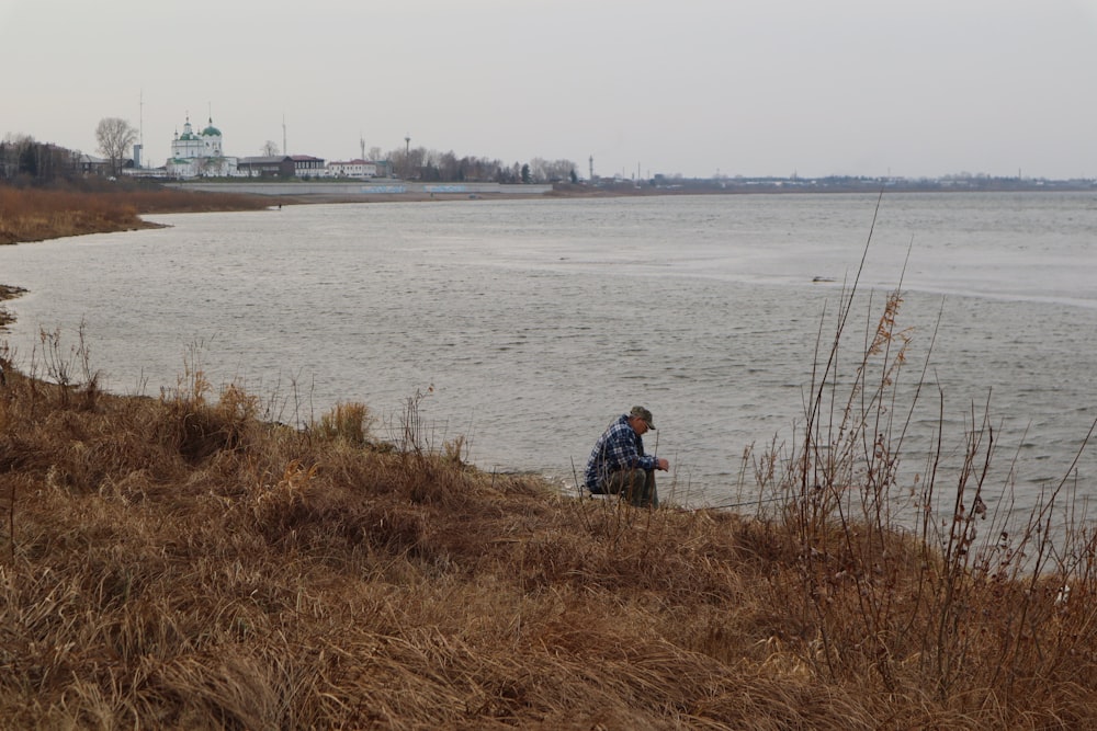 a man sitting on a hill next to a body of water