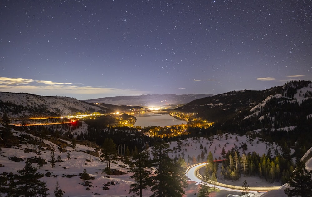 a night time view of a snowy mountain with a lake in the distance