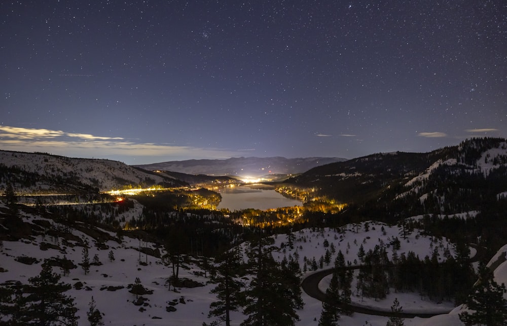 a night time view of a snowy mountain with a lake in the distance