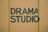 Bold green lettering spells out 'Drama Studio' against a muted yellow background, with visible texture and slight imperfections in the paint.