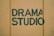 Bold green lettering spells out 'Drama Studio' against a muted yellow background, with visible texture and slight imperfections in the paint.