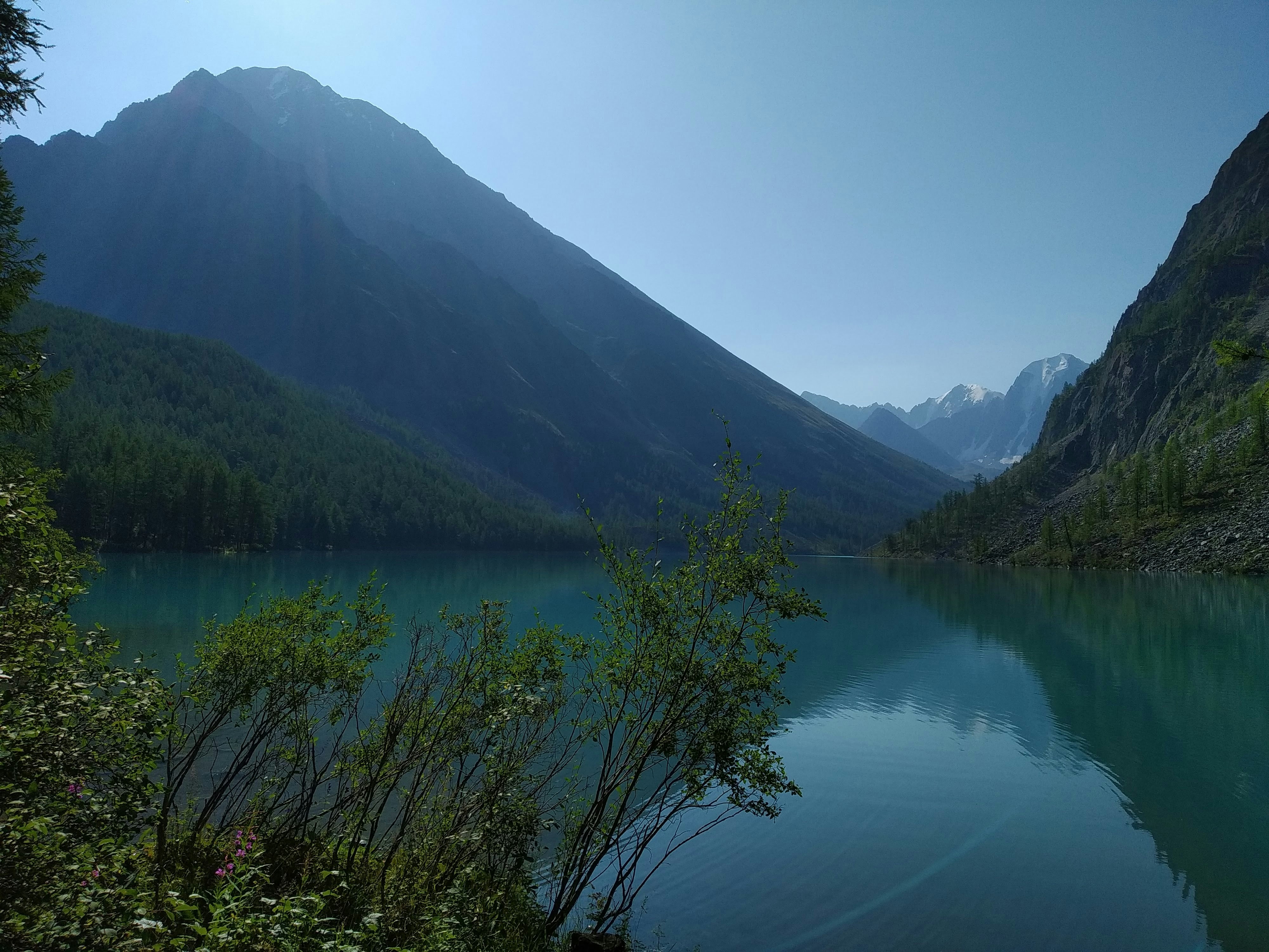 a lake surrounded by mountains and trees on a sunny day