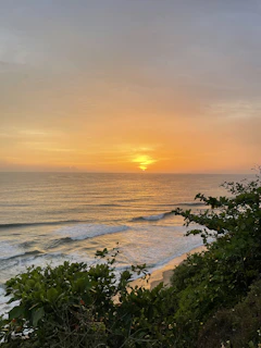 A serene Kona coastline at sunset with gentle waves and lush greenery.