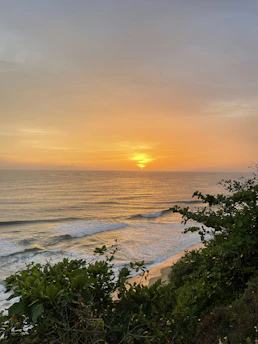 A serene Kona coastline at sunset with gentle waves and lush greenery.
