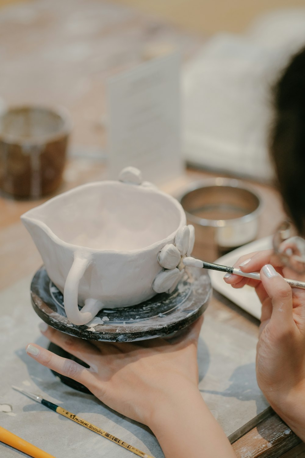 a woman is painting a white vase on a table