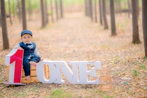 a young boy sitting on top of a one sign in the woods