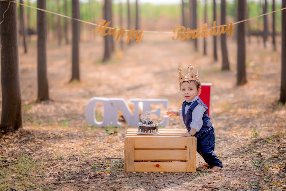 a young boy wearing a crown standing next to a cake