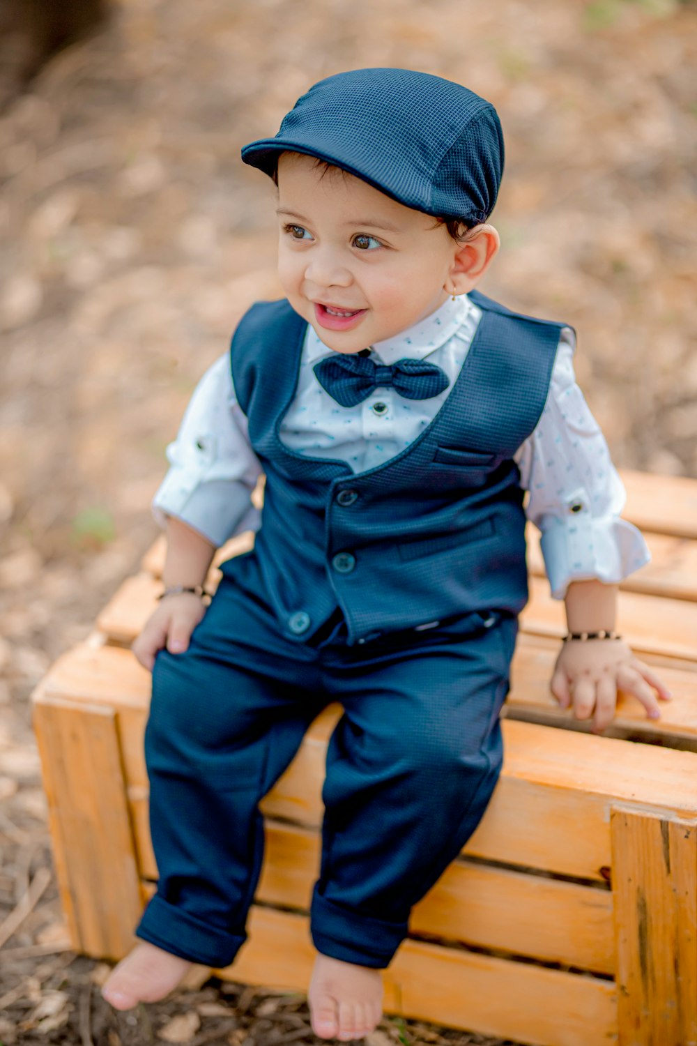 a young boy in a blue suit and hat sitting on a wooden bench