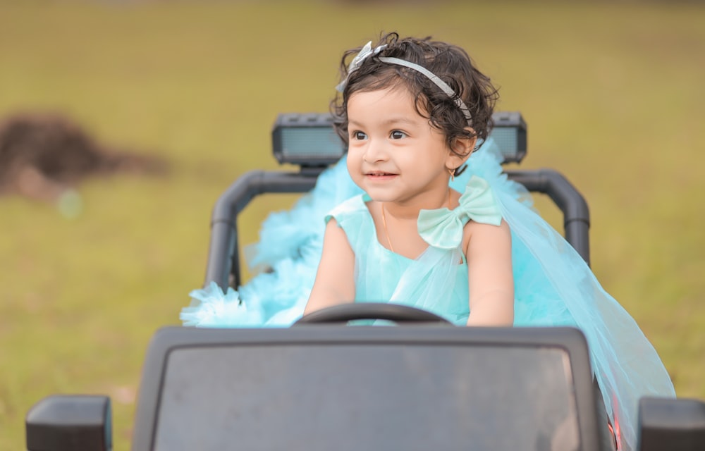 a little girl in a blue dress sitting in a buggy