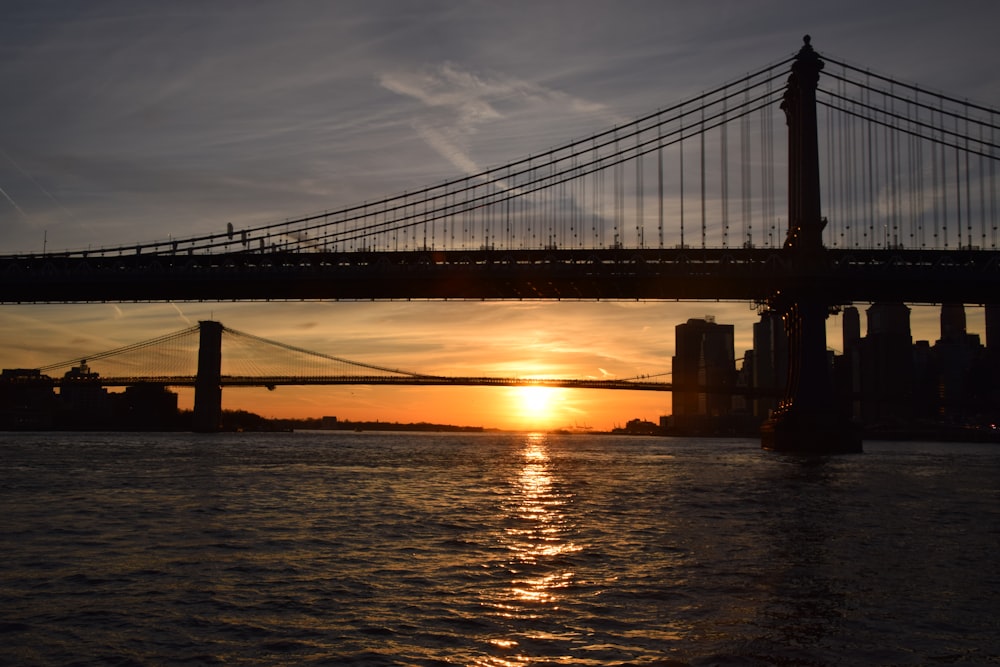 the sun is setting behind a bridge over a body of water