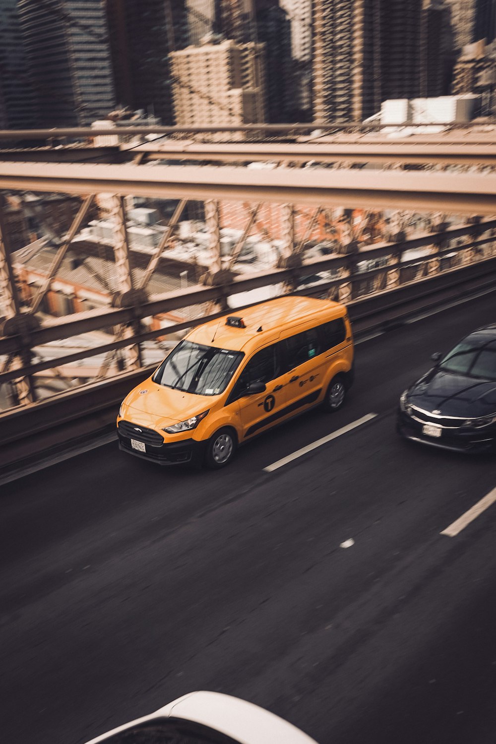 a yellow van driving down a street next to a black car