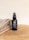 A bottle of beard oil with a dark label and pump dispenser is placed on a wooden surface next to folded towels. The label indicates it is enriched with vitamin E, argan oil, and macadamia oil.
