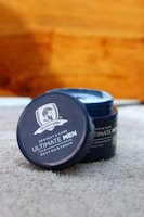 A jar of daily hair cream for men is placed open on a soft, textured surface. The product label features the brand 'The Beard Story' and emphasizes protection and care, indicating it is paraben-free.