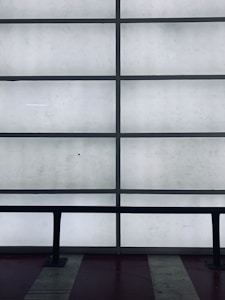 A grid of frosted glass panels is framed by dark metal bars, creating a minimalist architectural pattern. In front of the panels, a dark railing runs horizontally across the lower part of the image.