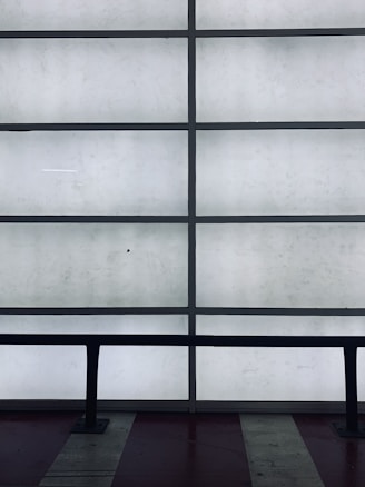 A grid of frosted glass panels is framed by dark metal bars, creating a minimalist architectural pattern. In front of the panels, a dark railing runs horizontally across the lower part of the image.