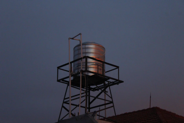 A sleek stainless steel fire water tank gleaming under bright sunlight beside a modern hospital building.
