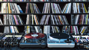 A collection of vinyl records spread out on a table with a turntable in the background.