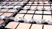 Multiple rectangular salt pans arranged in a grid pattern with dark embankments. The surfaces of the pans have varying shades of brown and beige with salt deposits accumulated at the edges.
