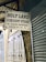 A sign for the Holy Land Discount Store, displaying the proprietor's name M. Nafez Shweiki, and address at David Street No. 61. The sign is hung in a dimly lit alleyway with closed metal shutters and weathered wall structures.